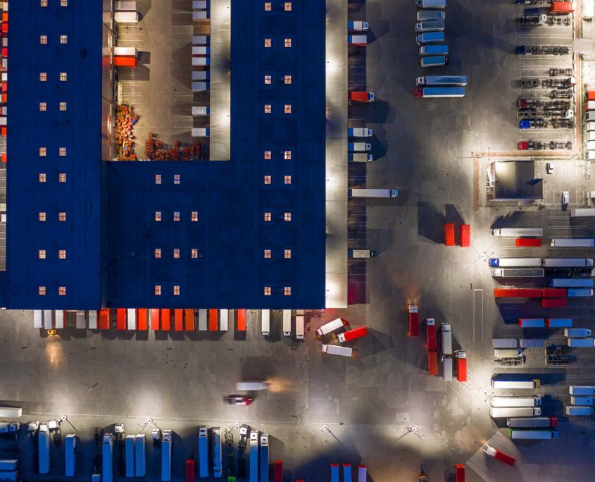 Aerial top down view view of a large logistics park with a warehouse. Semi-trailers trucks standing at ramps for loading and unloading goods at winter night